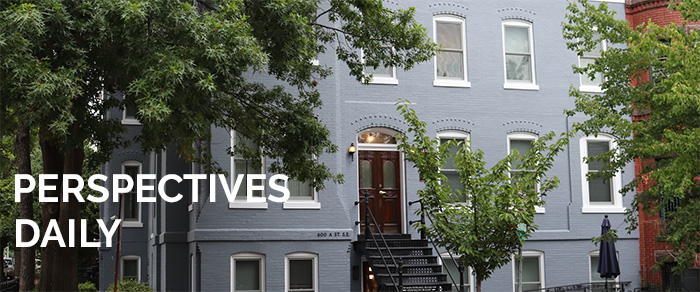 AHA townhouse, a blue brick buildng with a black iron stair case leading to a dark wooden door. Three trees with green leave are planted in front of the townhouse. 